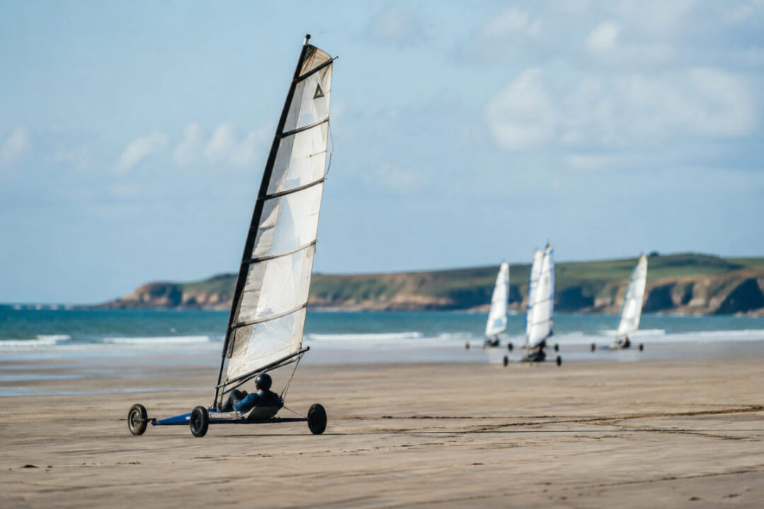 Pratiquants de char à voile Cotentin filant sur une grande plage à marée basse